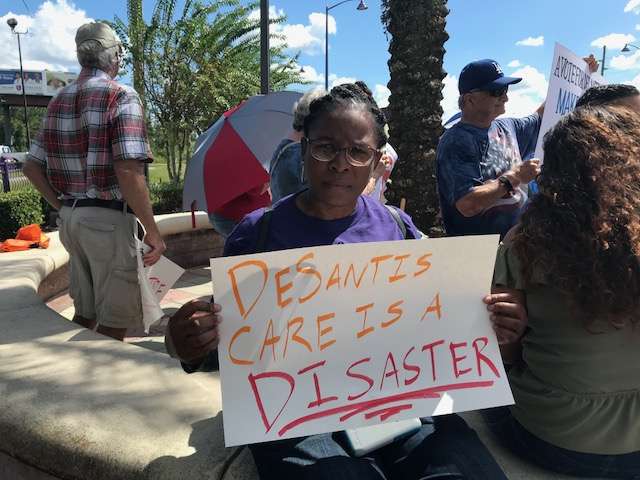 Protesters outside a Ron DeSantis campaign stop hold signs calling on healthcare coverage for all. Photo: Danielle Prieur